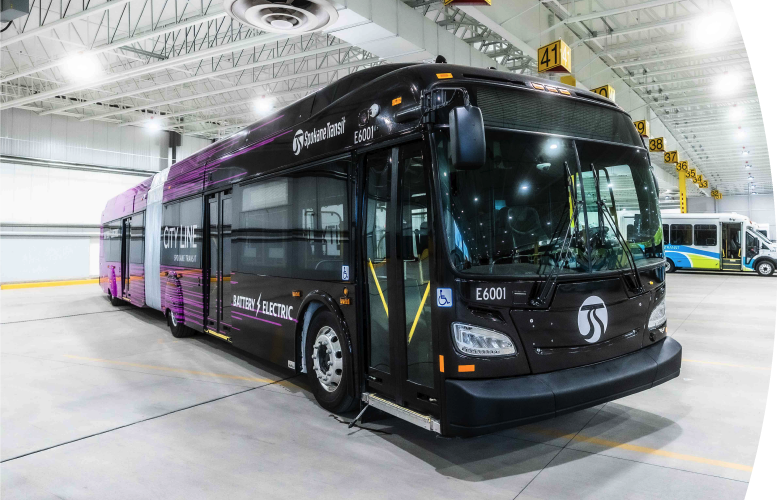 A modern articulated electric bus parked inside a spacious, well-lit transit facility, featuring sleek black and purple branding of "Spokane Transit.