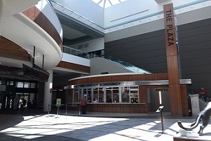 A modern plaza with a Spokane Transit security and photo service kiosk, featuring an open design with a high ceiling, large windows, and sunlight streaming in.