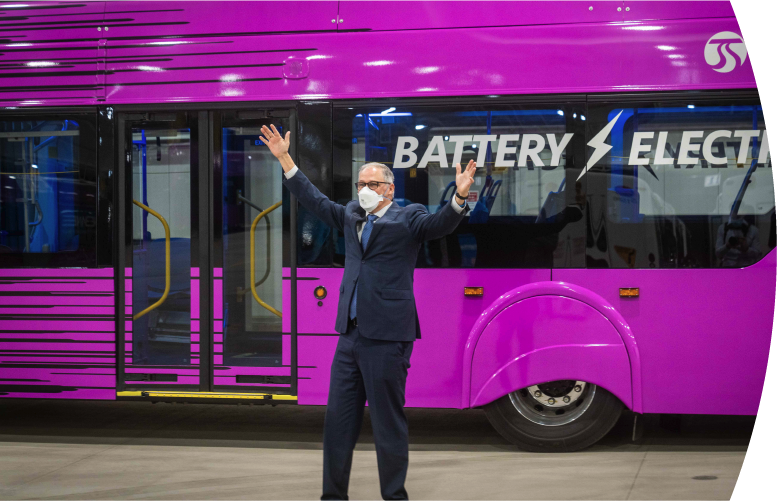 Governor Jay Inslee standing with his arms spread wide in front of a battery electric City Line rapid transit bus