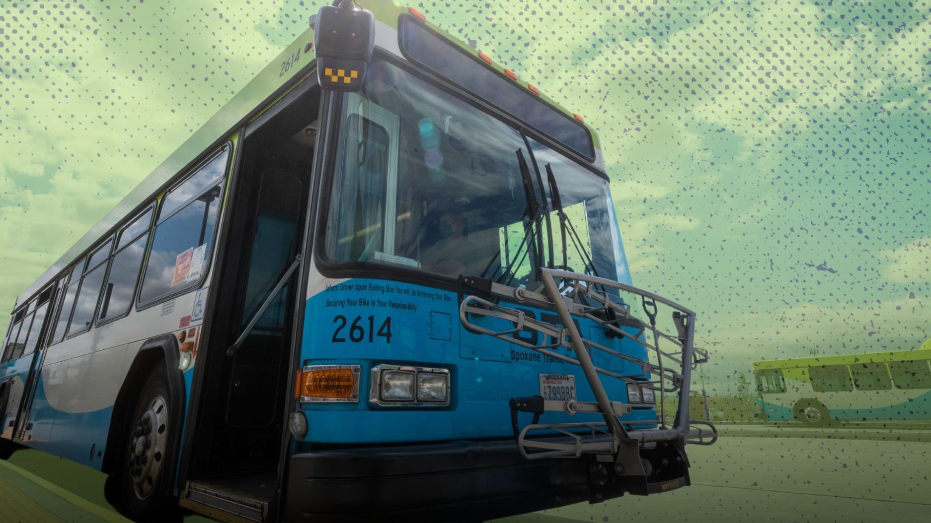 A city bus with route number 2614 is parked at a bus stop. It features a bike rack at the front and a greenish-blue exterior promoting Zero Fare for Youth. The sky is partly cloudy, and a smaller, similarly colored bus is visible in the background.