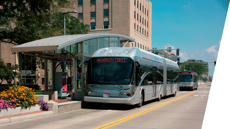 A silver bus with "Spokane Transit" displayed on its front, parked at a modern bus stop in an urban area with buildings and trees under a clear sky.