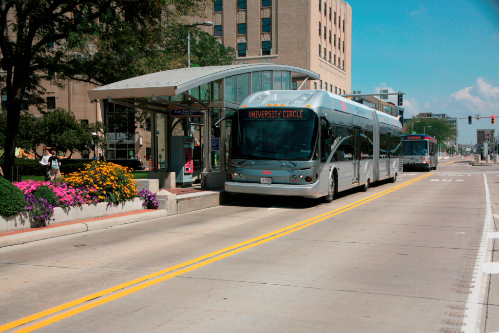 A modern bus with "Spokane Transit" signage stops at a designated bus station on a sunny day, bordered by vibrant flower beds alongside an urban road.