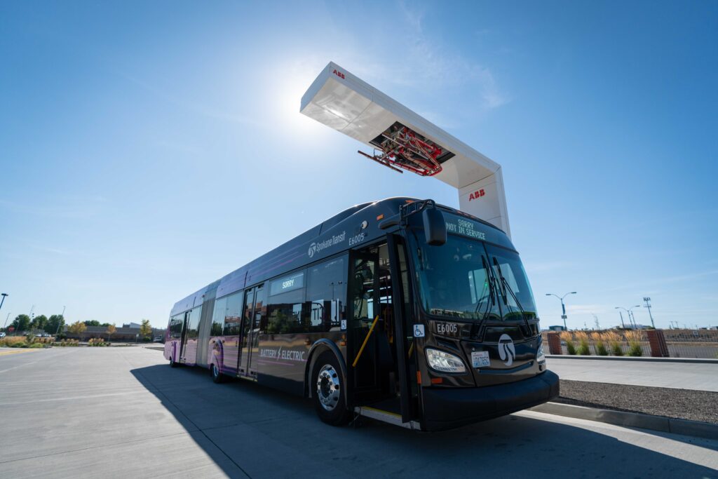 Electric bus docking at an outdoor charging station under a clear blue sky.