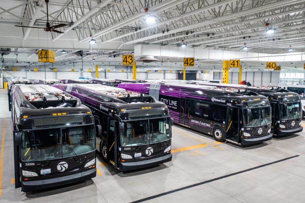 A group of buses parked inside a large, well-lit garage with numbered yellow signs overhead.