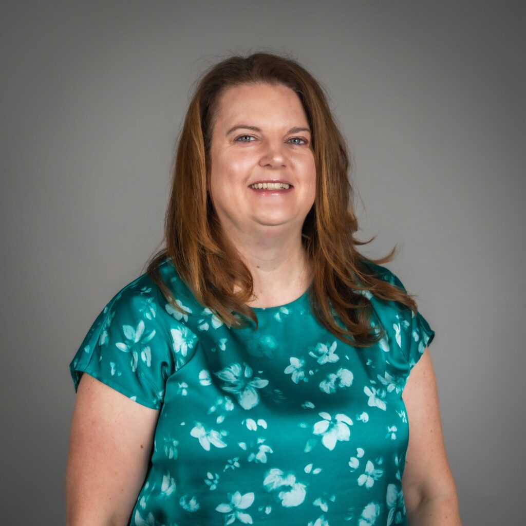 STA's Chief Communications Officer Carly Cortright in a teal floral blouse, smiling against a gray background.