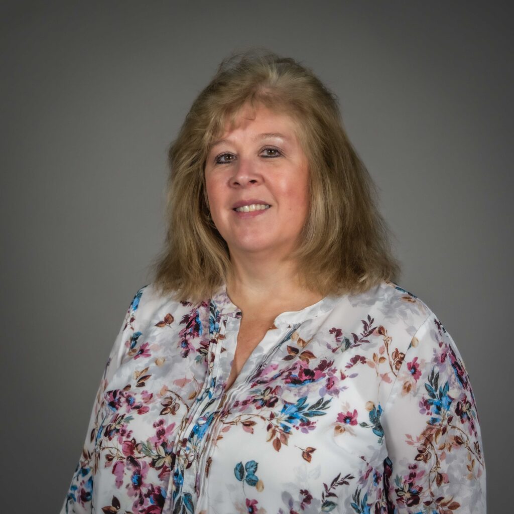 Interim Chief Financial Officer Tammy Johnson stands in a floral blouse, smiling against a plain background.