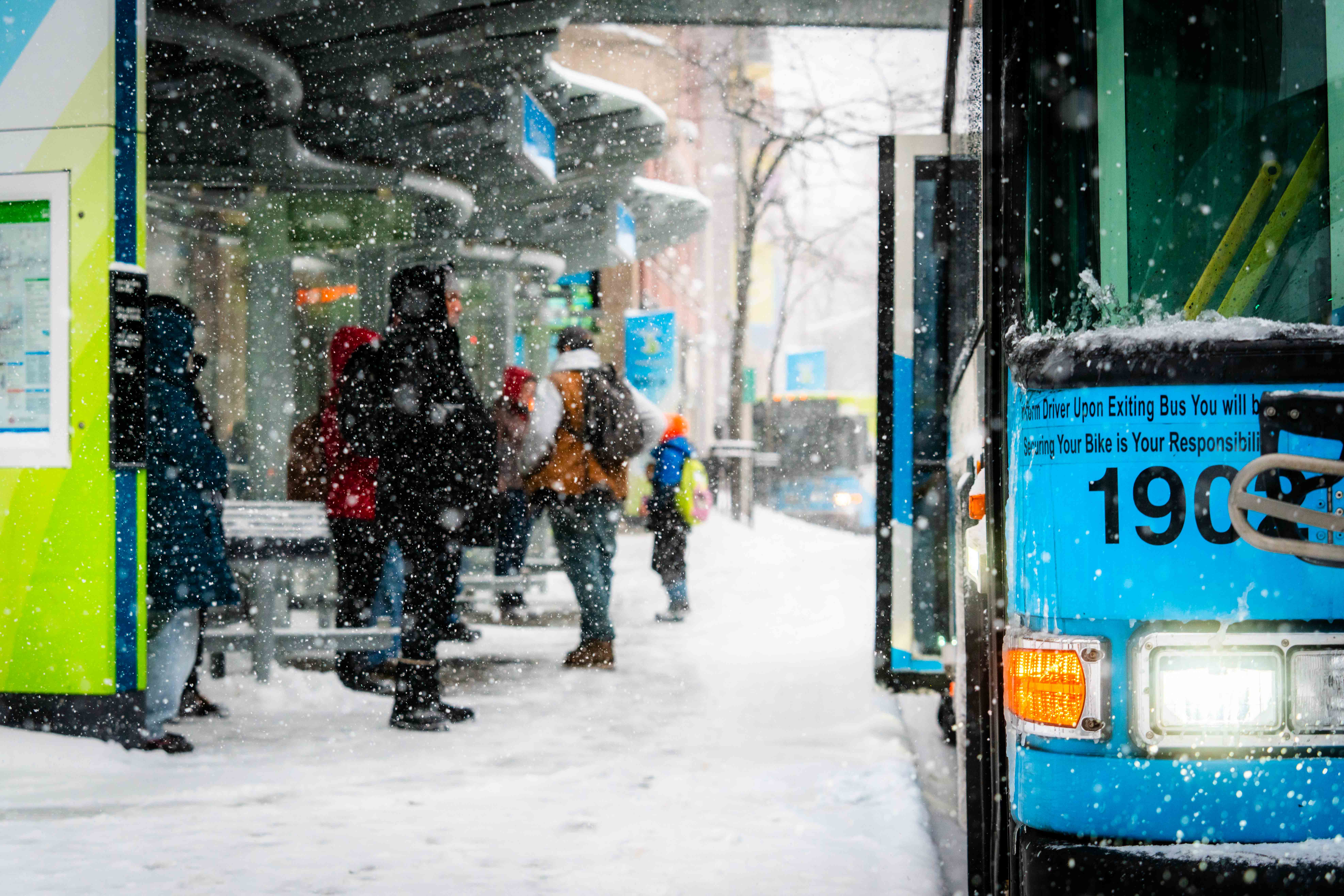 People waiting at a snowy bus stop as an STA bus arrives.