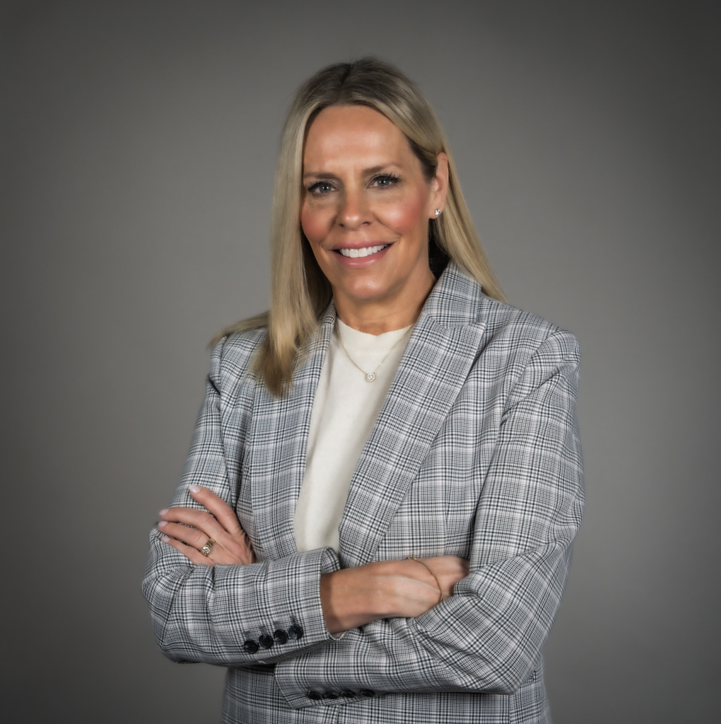 STA's Chief Human Resources Officer Nancy Williams with long blonde hair, in a plaid blazer, posing with arms crossed against a gray background.