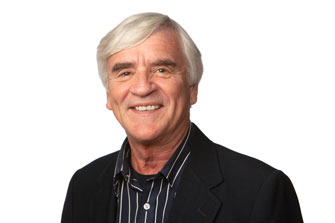 Smiling older man with white hair in a black jacket and striped shirt, against a white background.