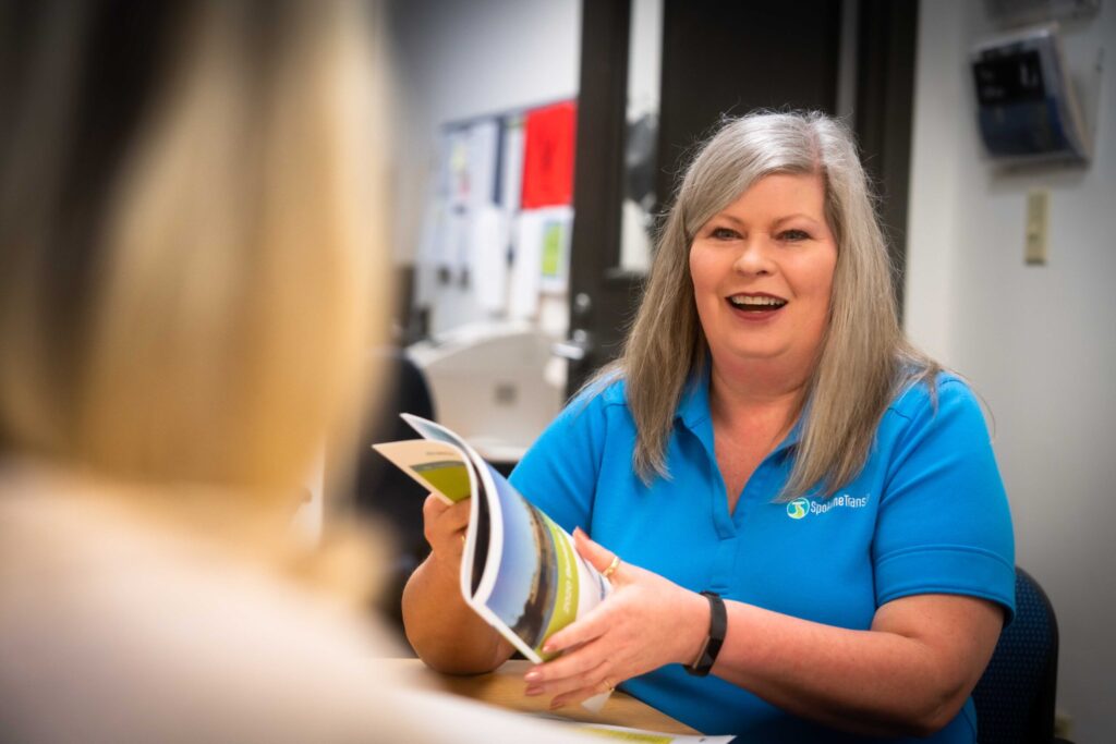 A woman in a blue shirt smiling and holding a brochure at a desk.