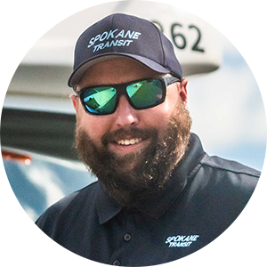 Man in "Spokane Transit" cap and sunglasses, smiling outdoors, with a bus in the background.