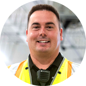 A person in a neon safety vest and black shirt smiling, wearing a communication device on their chest.