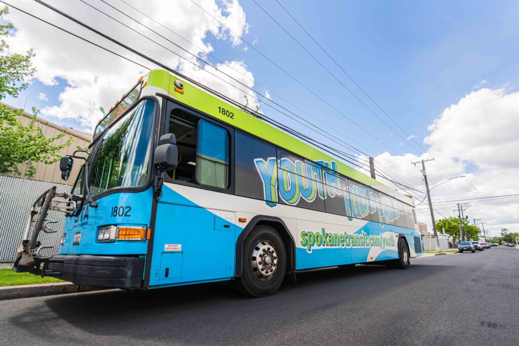 A blue and white STA bus featuring "youth kick pass" on its side is parked on a street.