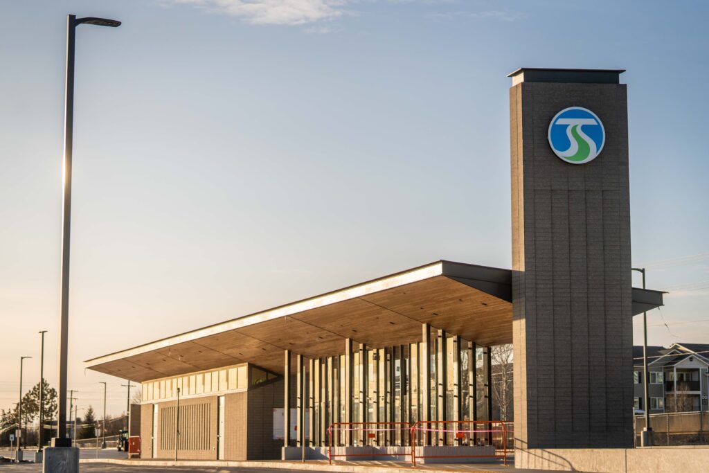 Modern building with large windows and a tall signpost under a clear sky, featuring a blue and green logo.