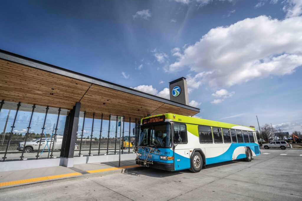 A blue and green bus parked at a modern transit station under a partly cloudy sky.