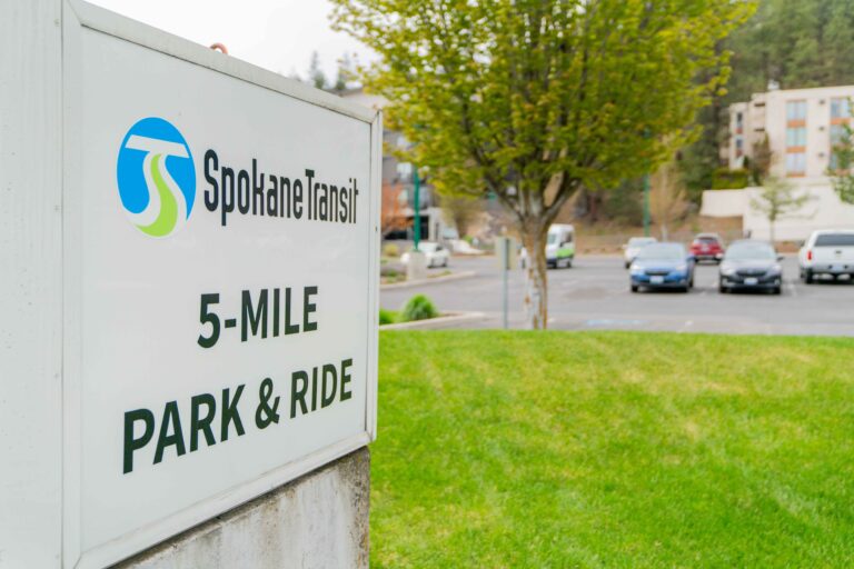 STA bus and "5-Mile Park & Ride" Spokane Transit sign by parking lot with cars and trees.