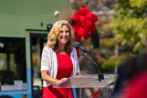 EWU President Shari McMahan speaks at the podium with the double-decker bus behind her.