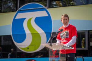 STA CEO Karl Otterstrom speaks at the podium in front of the double-decker bus.