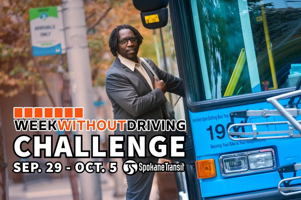 Man in a suit stands by a blue Spokane Transit bus for the Week Without Driving Challenge.
