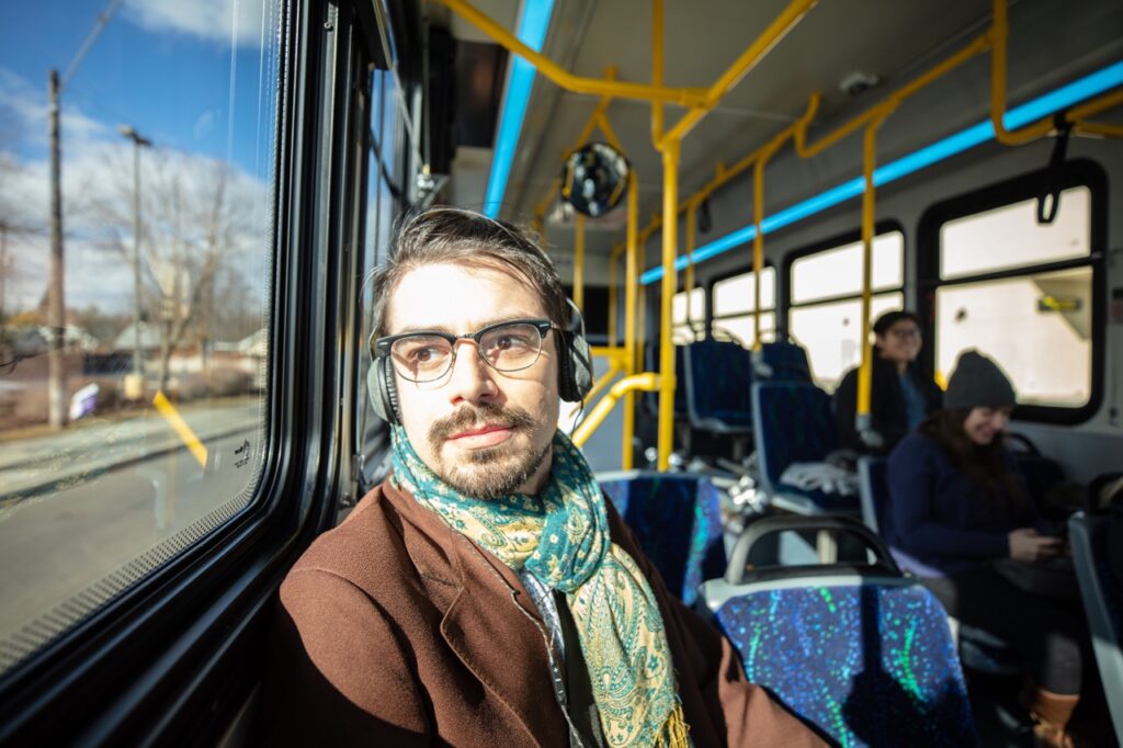 A man wearing glasses and headphones looks out a bus window.