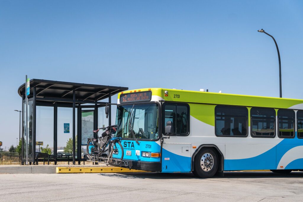 City bus with bike on front rack stops at a shelter.