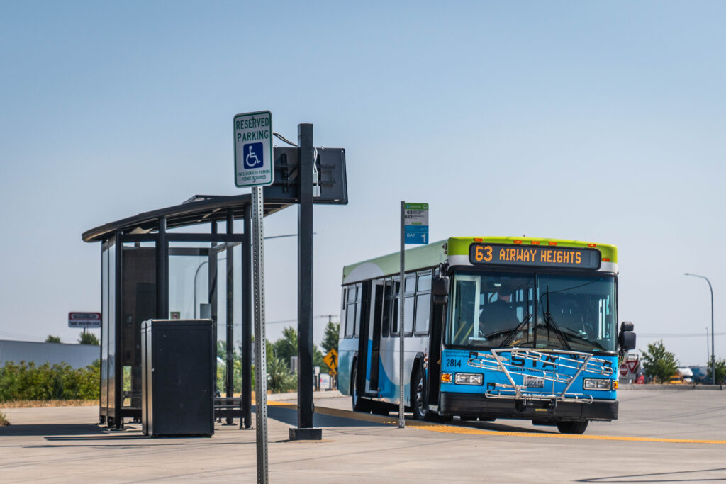 Blue city bus labeled "63 Airway Heights" at a shelter near a reserved parking sign.