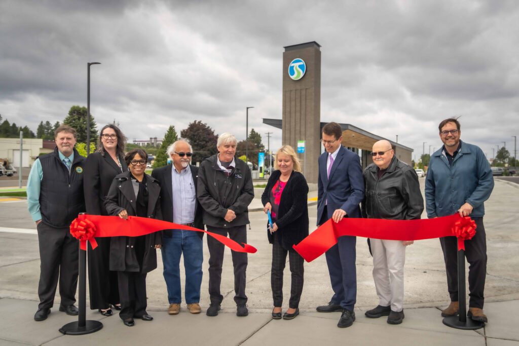 Nine people hold a red ribbon in front of a new building at a ribbon-cutting ceremony.