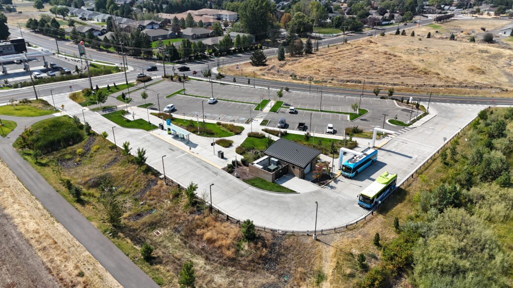 Aerial view of a blue bus at a charging station in a mostly empty parking lot.