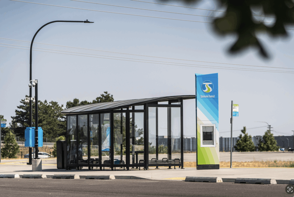 Modern glass bus shelter with Spokane Transit sign in an empty parking lot.