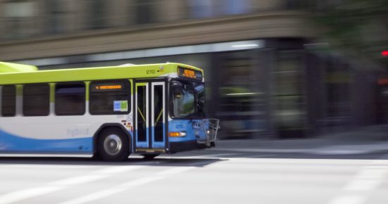 Blurred image of a moving city bus with a green and blue color scheme on a street.
