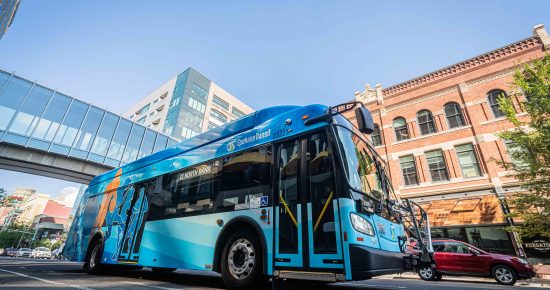 Blue STA bus with vibrant design on a street near modern and brick buildings under a clear sky.
