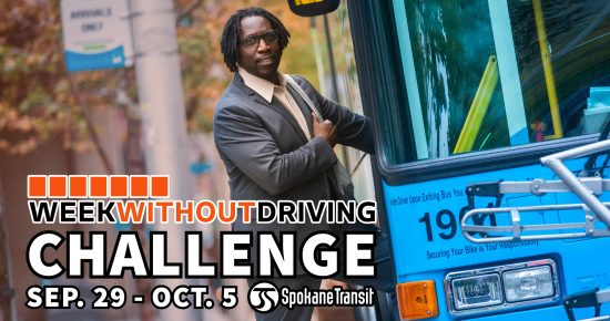 Man in a suit stands by a blue Spokane Transit bus for the Week Without Driving Challenge.