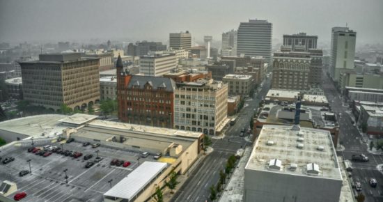 Aerial view of Spokane on a foggy day, featuring several mid-rise buildings and scattered parking lots, with a hazy skyline in the background.