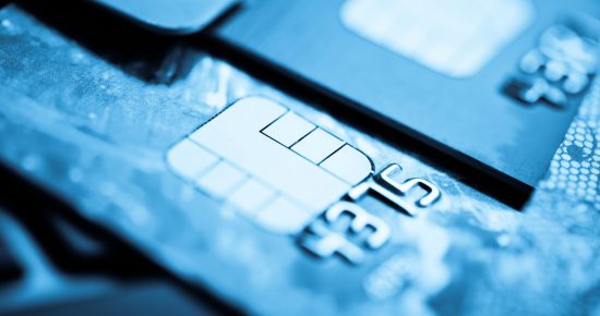 Close-up shot of multiple credit cards with electronic chips. The focus is primarily on the chip of one card, highlighting its metallic surface and intricate details. The background appears blurred, showing parts of other overlapping credit cards.